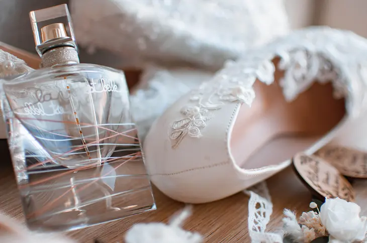 Accessoires de mariée disposés pêle-mêle comprenant une chaussure blanche avec dentelle, un parfum, des rubans - photo Urielle PENN photographe de mariage