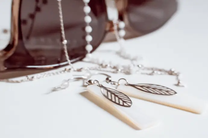 Paire de boucles d'oreilles en nacre posées devant une paire de lunettes de soleil ornée de colliers de perles - photo Urielle Penn photographe de mariage